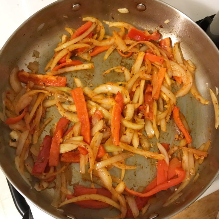 sliced onions and peppers sauteing in pan with spice mix
