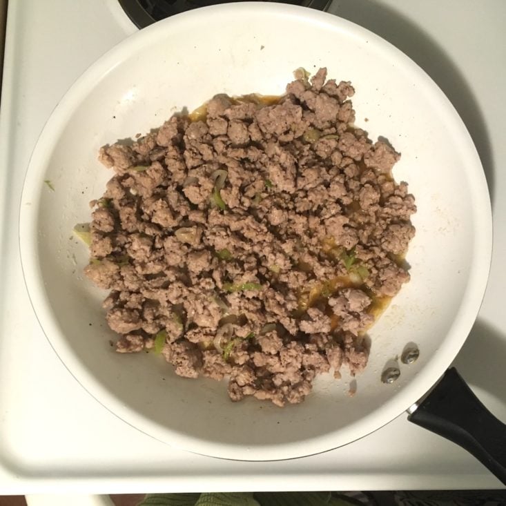 ground pork simmering with green onions in a large white skillet