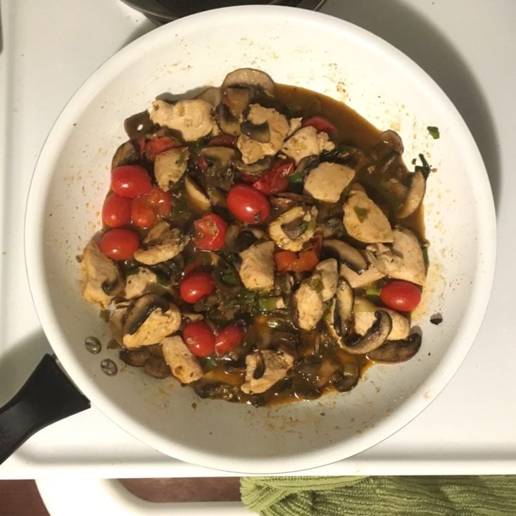 chicken and vegetables cooking in a large, white skillet for the cajun grits recipe with a demi-glace