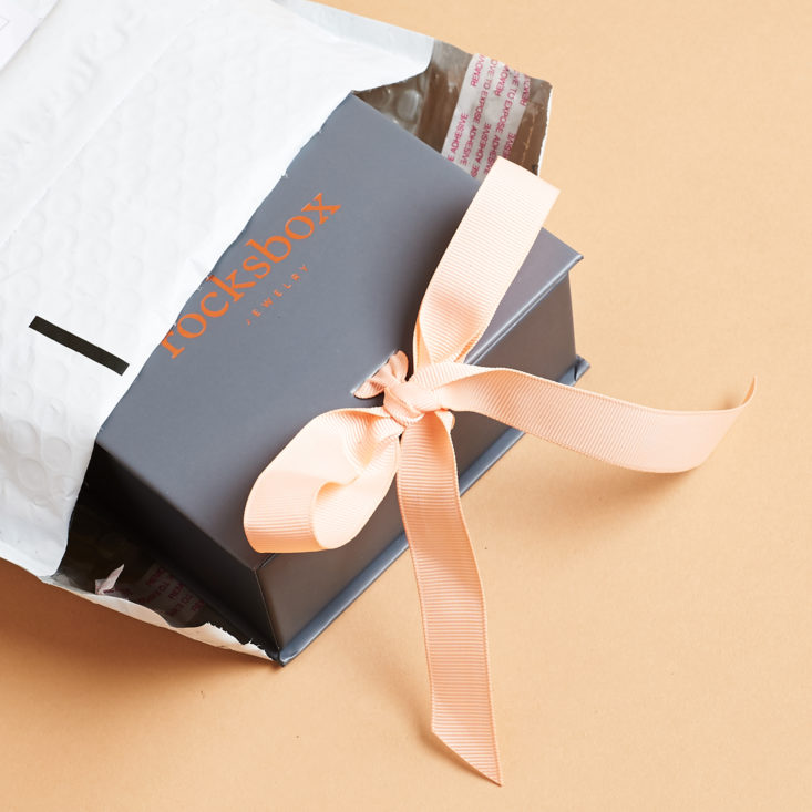 open envelope showing grey box with pink ribbon