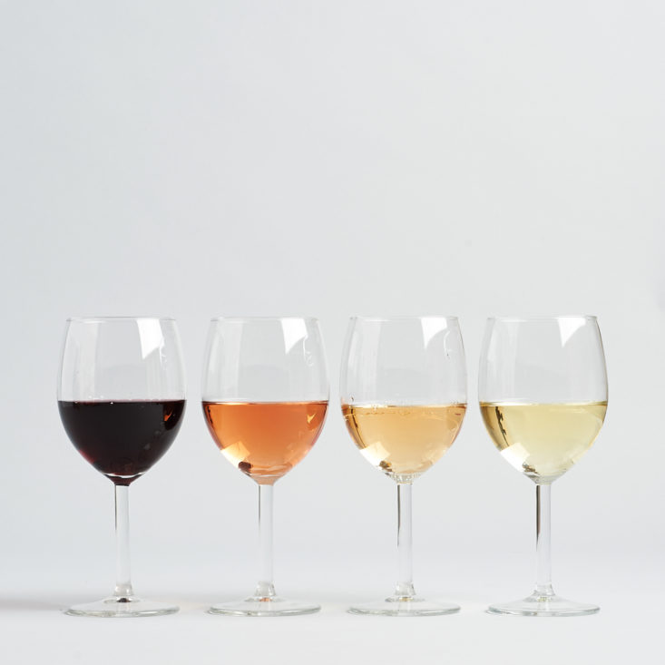 four individual glasses filled with different wines from darkest to lightest